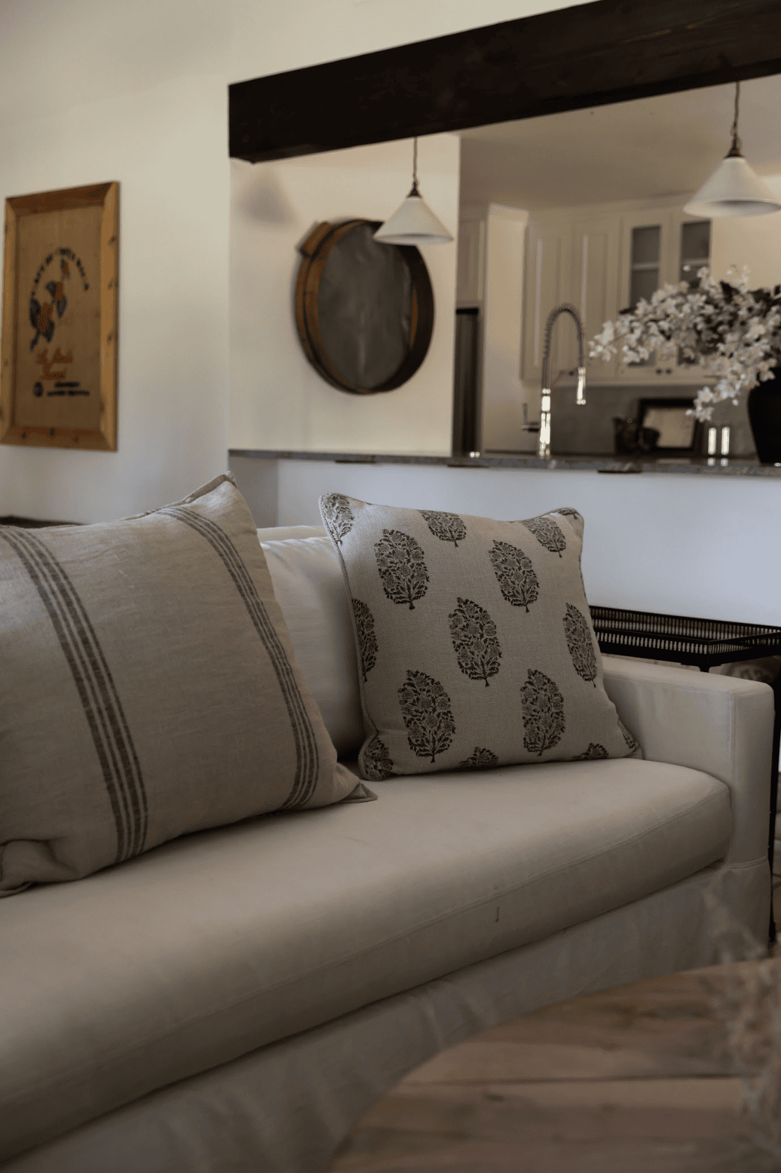 Linen sofa with patterned pillows beneath a dark wood beam