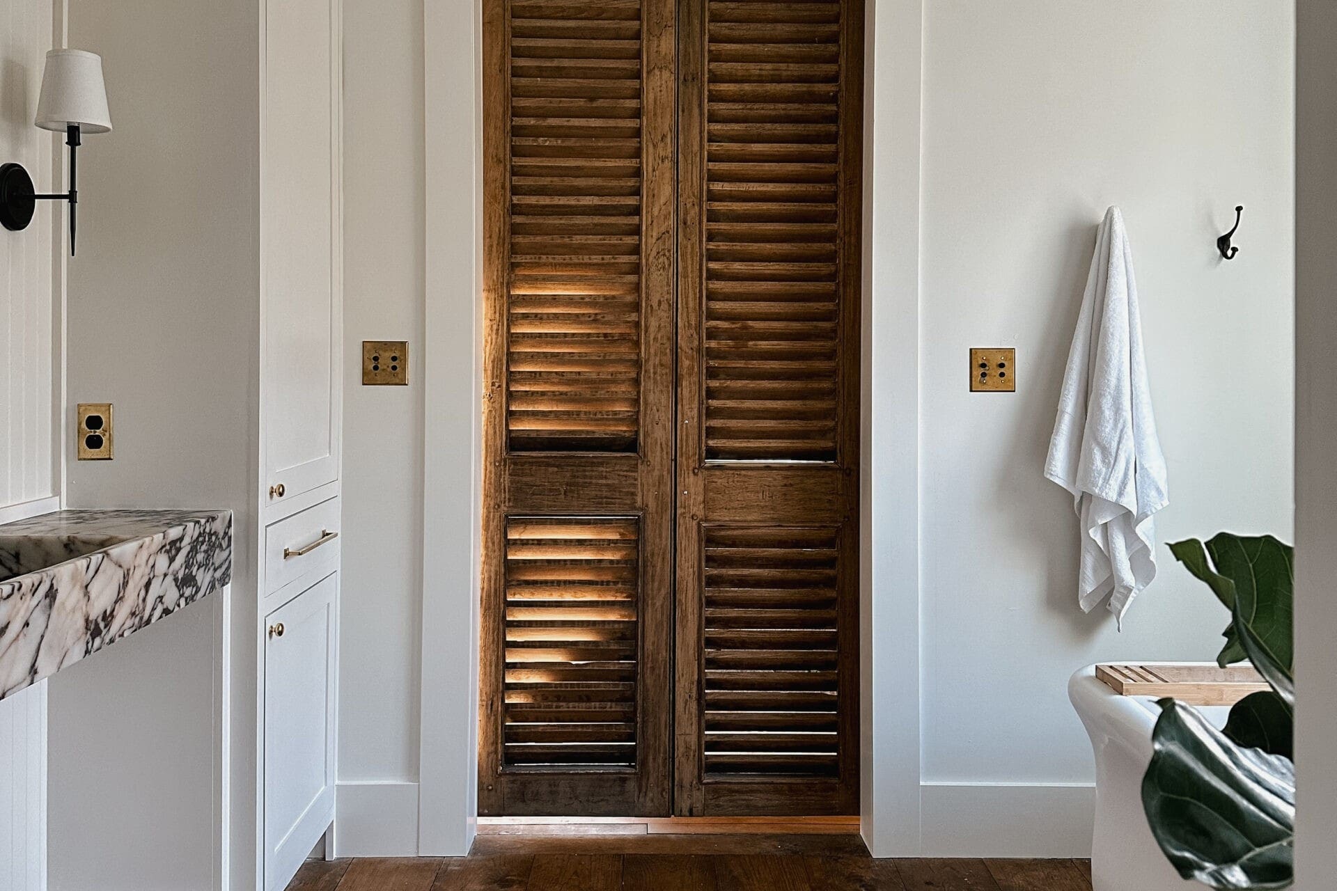 European farmhouse bathroom with a louvered wood door and wide plank floors